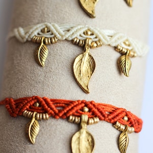 May include: Four layered bracelets with gold leaf charms. The bracelets are made of brown, white, orange, and red cord.