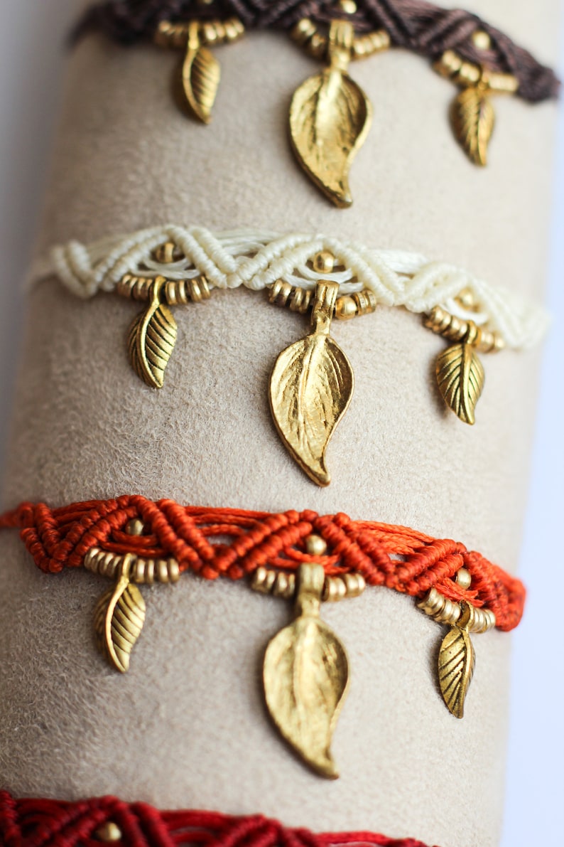 May include: Four layered bracelets with gold leaf charms. The bracelets are made of brown, white, orange, and red cord.