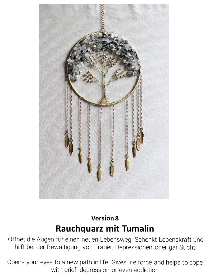 May include: A gold-toned metal dreamcatcher with a circular frame and a tree of life design. The tree is adorned with clear and gray crystals. The dreamcatcher has multiple strands of beads and feathers hanging from the bottom.