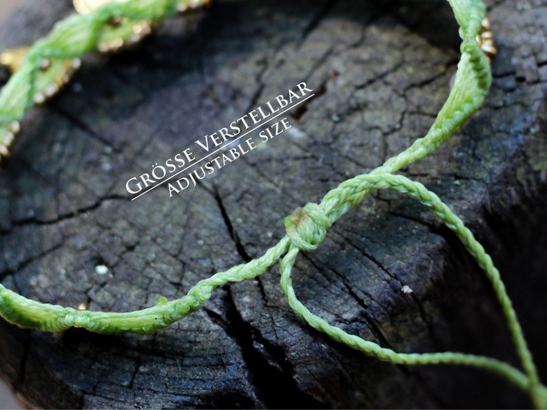 May include: A green braided cord bracelet with gold beads. The bracelet is adjustable and has a knot at the end. The text "GR&Ouml;SSE VERSTELLBAR ADJUSTABLE SIZE" is printed on the bracelet.