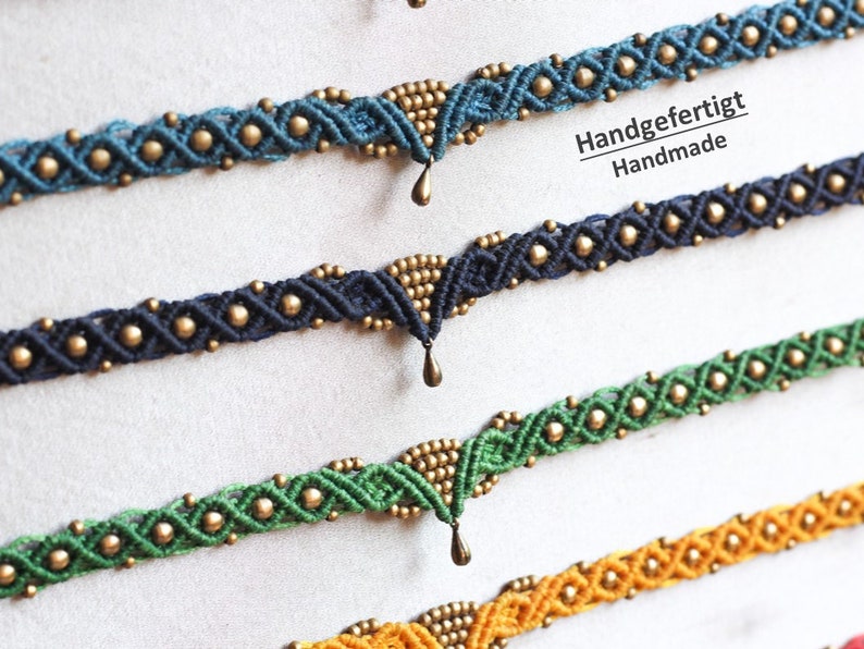 May include: Four handmade macrame bracelets with gold beads and a dangling charm. The bracelets are in shades of blue, green, and yellow. The text "Handgefertigt Handmade" is visible in the image.