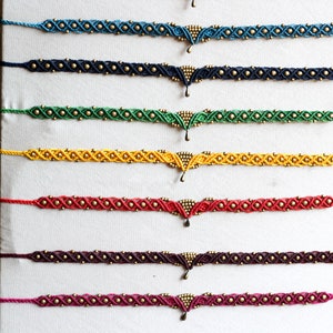May include: A set of eight colorful friendship bracelets with gold beads and a gold pendant. The bracelets are displayed on a white background.