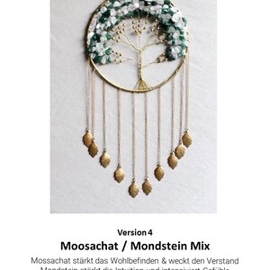 May include: A gold wire tree of life dreamcatcher with moss agate and moonstone crystals. The dreamcatcher has a circle frame with a beaded wire tree and hanging gold leaves. The text "Version 4 Moosachat / Mondstein Mix" is below the dreamcatcher. Mossachat strengthens well-being and awakens the mind. Moonstone strengthens intuition and intensifies feelings.