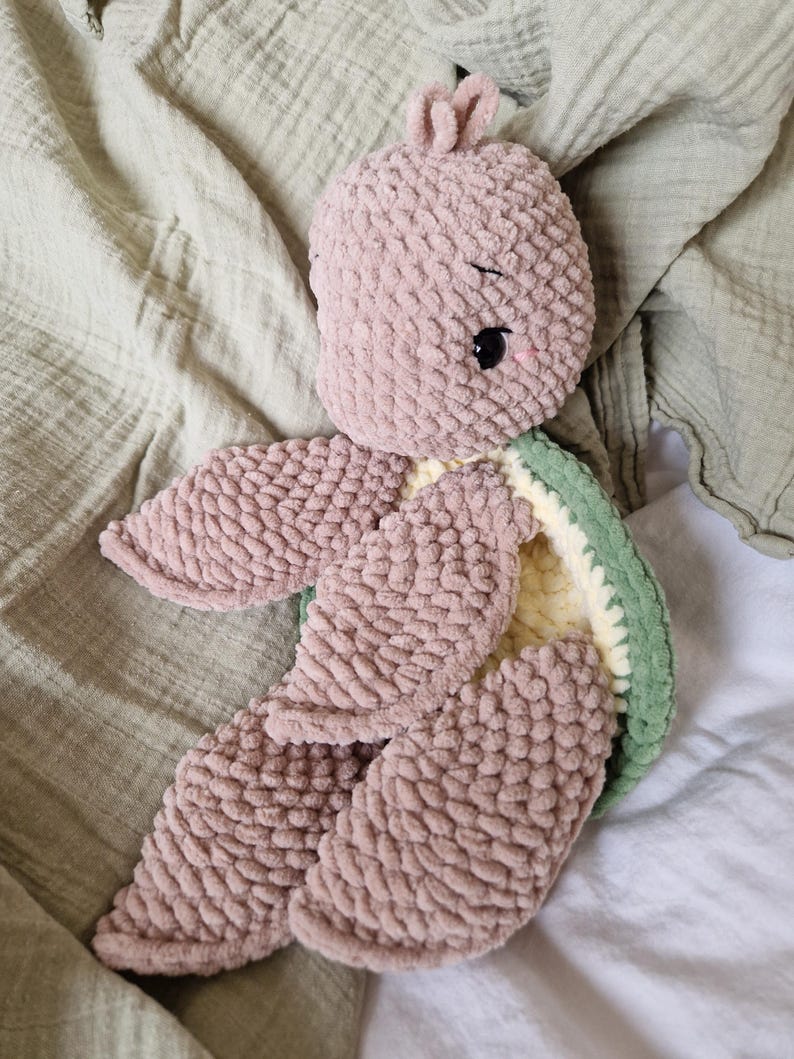 May include: A crocheted plush turtle toy with a pink body, green shell, and yellow accents. The turtle has a sweet expression with black eyes and pink cheeks.