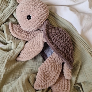 May include: A crocheted plush toy turtle in shades of brown and beige. The turtle has a soft, textured surface and a sweet, cartoon-like face.