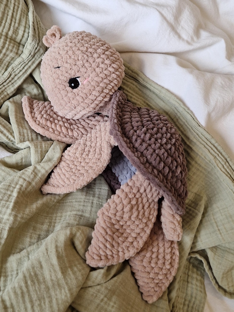 May include: A crocheted plush toy turtle in shades of brown and beige. The turtle has a soft, textured surface and a sweet, cartoon-like face.