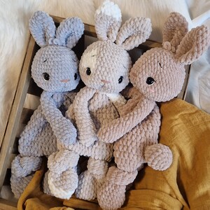 Puede incluir: Tres peluches de conejo de crochet en una caja de madera. Un conejo es gris claro, otro es marr&oacute;n claro y el &uacute;ltimo es una mezcla de marr&oacute;n claro y blanco.