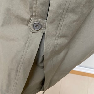 May include: A close-up of the back of a khaki-colored jacket with a single button closure. The jacket has a center back seam and two side seams.