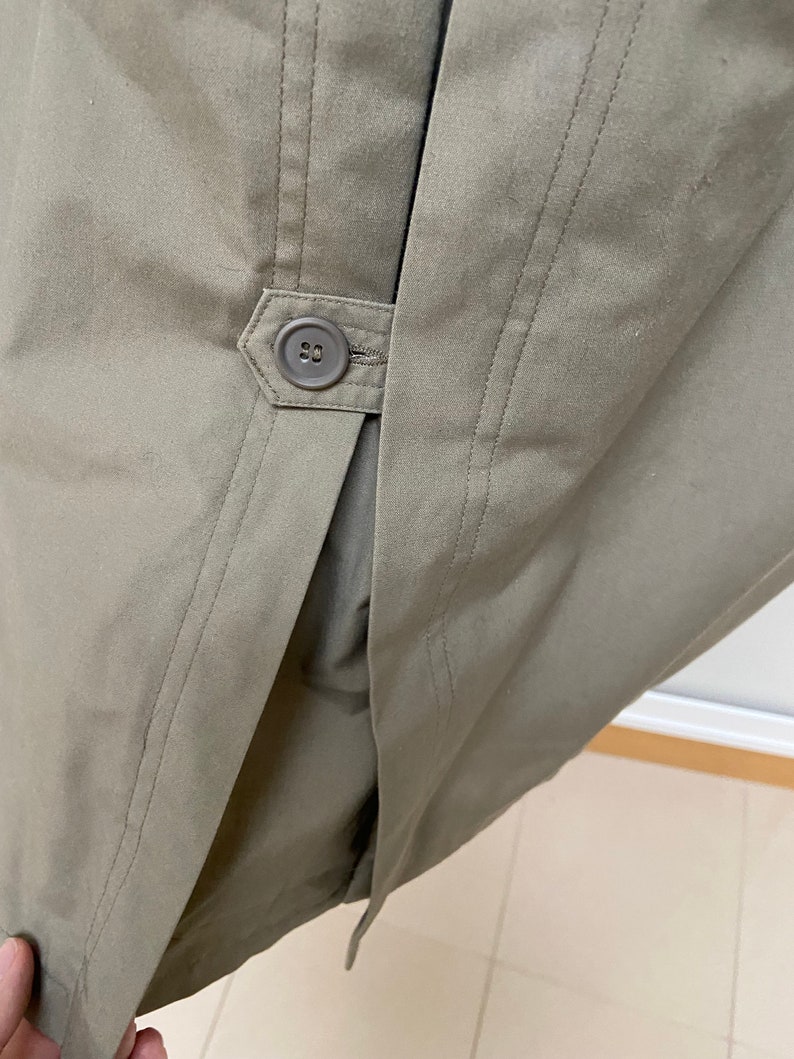 May include: A close-up of the back of a khaki-colored jacket with a single button closure. The jacket has a center back seam and two side seams.