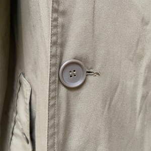 May include: A close-up of a brown button on a khaki jacket. The button has two holes.