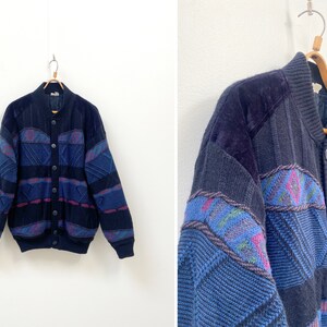 May include: A blue and purple patterned cardigan with a button-up front and a ribbed collar. The cardigan has a geometric design and is made of a soft, knitted fabric.