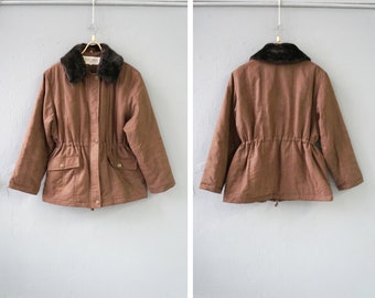 Könnte beinhalten: Eine braune Jacke mit einem Kunstfellkragen. Die Jacke hat einen Kordelzug in der Taille und zwei Taschen.