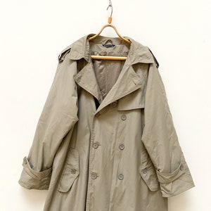 May include: A long, beige trench coat with a double-breasted closure and a belt. The coat has a classic design with a collar, pockets, and a buttoned cuff.
