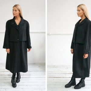 May include: A long black coat with a green lining and a contrasting collar. The coat has a double-breasted closure and a long, flowing silhouette.