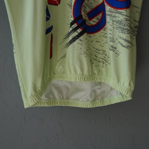 May include: A light green shirt with a blue, red, and black graphic print. The shirt has a drawstring at the bottom.