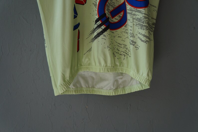 May include: A light green shirt with a blue, red, and black graphic print. The shirt has a drawstring at the bottom.