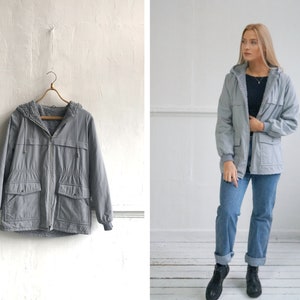 Op de afbeelding: Een grijze capuchontrui met een fleecevoering. De trui heeft een ritssluiting, twee zakken en een capuchon met trekkoord.