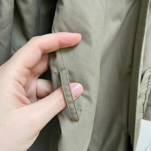 May include: Close-up of the inside of a khaki green jacket showing a small fabric loop sewn into the seam.