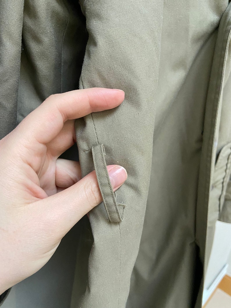 May include: Close-up of the inside of a khaki green jacket showing a small fabric loop sewn into the seam.