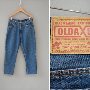 Puede incluir: Un par de pantalones vaqueros azules con un parche de cuero marrón en el bolsillo trasero. El parche tiene el texto "OLDAXE HARD WEARING EASY GOING" y "FROM THE FAMOUS OLDAXE MINING COUNTRY the trusty Oldaxe mules. YOU CAN ALWAYS BE SURE OF "our good old" HARD WEARING OLDAXE JEANS".