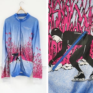 Könnte beinhalten: Eine blaue und rosafarbene Jacke mit langen Ärmeln und Reißverschluss. Die Jacke hat einen grafischen Aufdruck einer Person beim Eislaufen. Der Text "LES 1000 KM DE LA GORGONNE" ist auf der Jacke aufgedruckt.