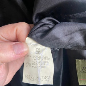 Pode incluir: Uma etiqueta de tecido branco com texto preto que detalha a composi&ccedil;&atilde;o do tecido de uma pe&ccedil;a de roupa. A etiqueta diz: 50% Schuriolle Laine Vierge Virgin Wool, 25% Kaschmir, 25% Polyamid. A etiqueta tamb&eacute;m inclui uma etiqueta de cuidados com s&iacute;mbolos para lavagem a seco, engomar e branquear.