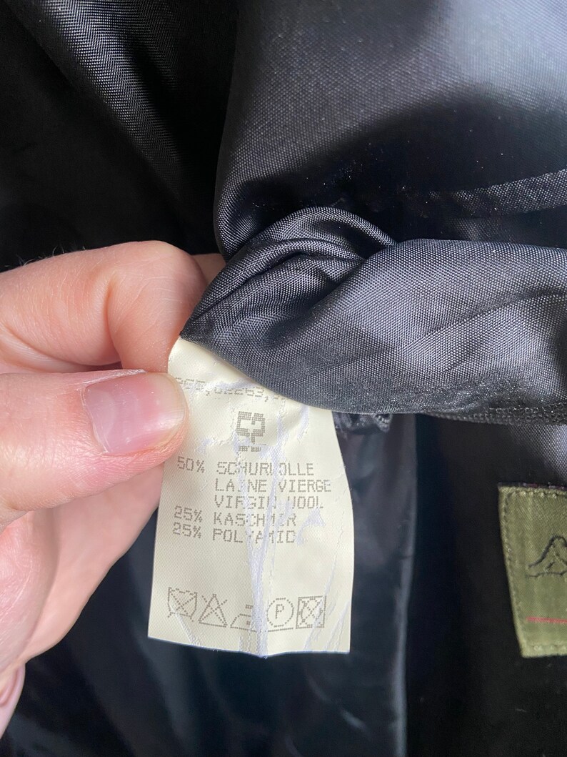 Pode incluir: Uma etiqueta de tecido branco com texto preto que detalha a composi&ccedil;&atilde;o do tecido de uma pe&ccedil;a de roupa. A etiqueta diz: 50% Schuriolle Laine Vierge Virgin Wool, 25% Kaschmir, 25% Polyamid. A etiqueta tamb&eacute;m inclui uma etiqueta de cuidados com s&iacute;mbolos para lavagem a seco, engomar e branquear.