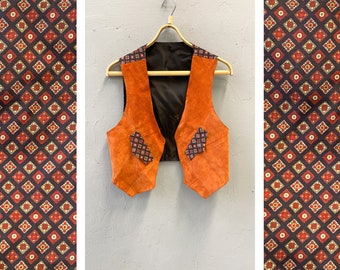 Könnte beinhalten: Eine braune Wildlederweste mit geometrischem Muster am Saum. Die Weste hat einen V-Ausschnitt und zwei Taschen.