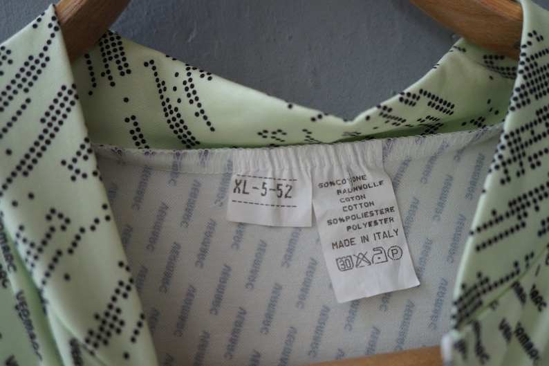 May include: A light green shirt with a black polka dot pattern. The shirt has a white tag with the text "XL-5-52", "SONCOTONE", "RAUNWOLLE", "COTTON", "SONPOLIESTERE", "POLYESTER", "MADE IN ITALY", and washing instructions.
