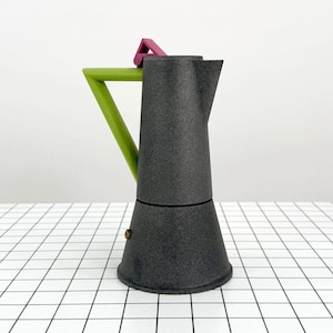 以下が含まれることがあります： 緑色のハンドルとピンク色のフリップアップ蓋が付いた、濃い灰色のエスプレッソメーカー。 コーヒーポットは三角形のハンドルとクラシックなデザインで、自宅でエスプレッソを淹れるのに最適です。