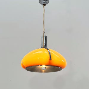 May include: A pendant light fixture featuring a vibrant orange, rounded glass shade held by a polished chrome metal frame. The fixture hangs from a thin cord attached to a chrome ceiling canopy, with a single light bulb visible inside the base.
