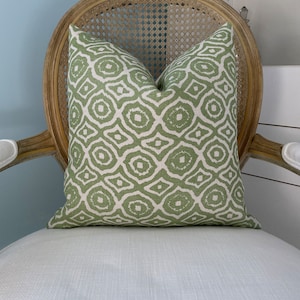 May include: A green and white patterned throw pillow on a white wicker chair. The pillow has a geometric design with a subtle sheen.