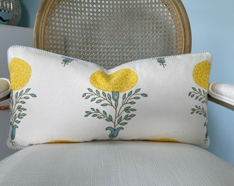 May include: A white lumbar pillow with a blue trim and a yellow floral print. The pillow is sitting on a white wicker chair.