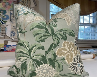 May include: A light blue cushion with a floral pattern in shades of green, brown, and white. The cushion has a subtle sheen and a soft, textured fabric.
