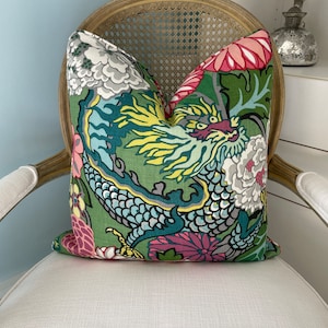 May include: A green, pink, and blue throw pillow with a dragon and floral pattern. The pillow is sitting on a white wicker chair.