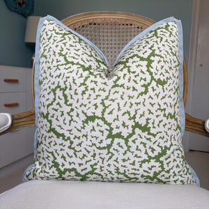 May include: A square throw pillow featuring a white fabric base with an organic, branching green pattern. The pillow is finished with a light blue flange border along all four edges, providing a distinct contrast to the green and white print.