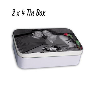 May include: A white rectangular tin box with a black and white photo of a couple on the lid. The photo shows a man and a woman smiling at the camera. There is a red rose in the background.