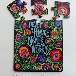 May include: A 12-piece jigsaw puzzle with a floral design and the words "Never Hurry Never Worry" on a black background. The puzzle pieces are arranged in a rectangle shape.