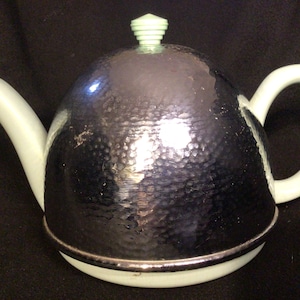 May include: A silver teapot with a domed lid and a light green handle and knob. The teapot has a hammered metal finish.