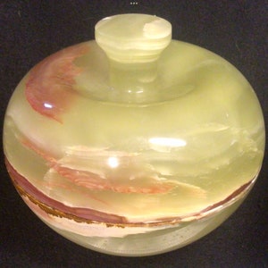 May include: A round, green, white and pink onyx trinket box with a lid. The box has a swirling pattern of colour.