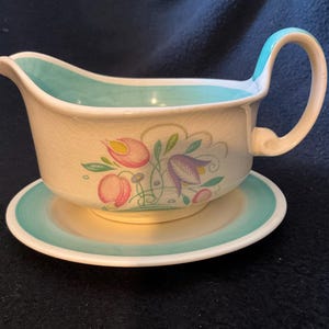 May include: A white ceramic gravy boat with a turquoise rim and floral design. The boat has a matching saucer.