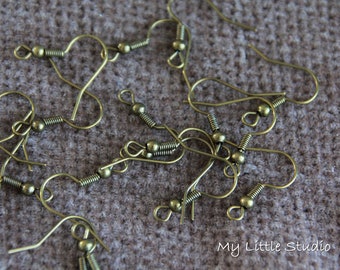 May include: A collection of antique brass-coloured earring hooks, scattered on a textured brown surface. The hooks feature a curved design with a coiled spring and a small ball. The image is well-lit, showing the details.