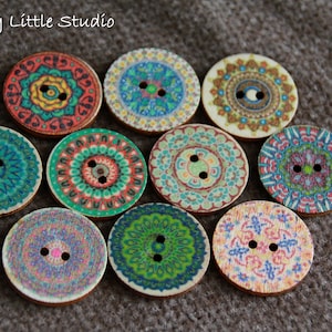 Könnte beinhalten: Zehn runde Holzknöpfe mit aufwendigen, farbenfrohen Mandala-Designs. Jeder Knopf zeigt ein einzigartiges Muster in Türkis, Orange, Grün und Lila. Die Knöpfe haben zwei Löcher zum Annähen und liegen auf einer strukturierten, braunen Oberfläche.