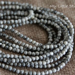 May include: Close-up of strands of grey and white marble beads. The small, round beads have a marbled pattern. They are strung together, suitable for a necklace or bracelet. The background is a neutral brown.