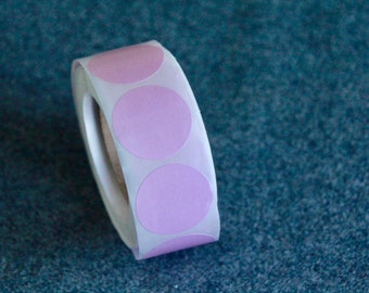 May include: A roll of round, light purple stickers. The stickers are on a white backing and are evenly spaced. The roll is partially unrolled, revealing the adhesive side. The background is a textured, dark blue surface.