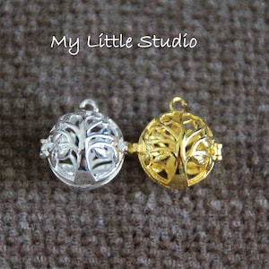 May include: Two spherical pendants, one silver and one gold, each featuring a tree of life design. The pendants are connected and rest on a textured brown surface. The text "My Little Studio" is in the upper left.