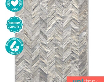 May include: White cowhide rug with a chevron pattern. The rug is made from ethically sourced materials and is of premium quality. The rug is made by up!rfnry.