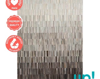 May include: A gray and white patchwork rug made from ethically sourced leather. The rug has a gradient pattern with darker shades at the bottom and lighter shades at the top. The rug is labeled "Ethically Made", "Premium Quality", and "Responsibly Sourced Materials".