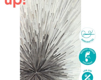 May include: A gray and white cowhide rug with a starburst pattern. The rug is handcrafted and has a reduced carbon footprint. The text "up!" is in the top left corner of the image.
