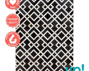May include: Black and white geometric patterned cowhide rug with a white border. The rug is made of ethically sourced materials and is of premium quality.